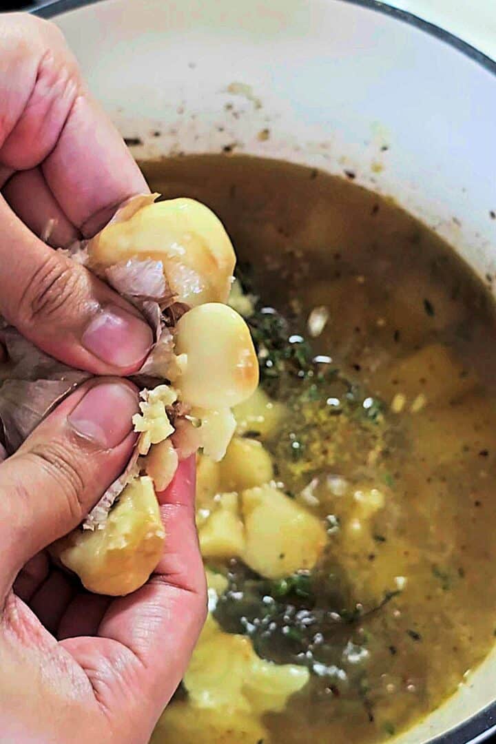 Roasted garlic cloves being squeezed into the pot.