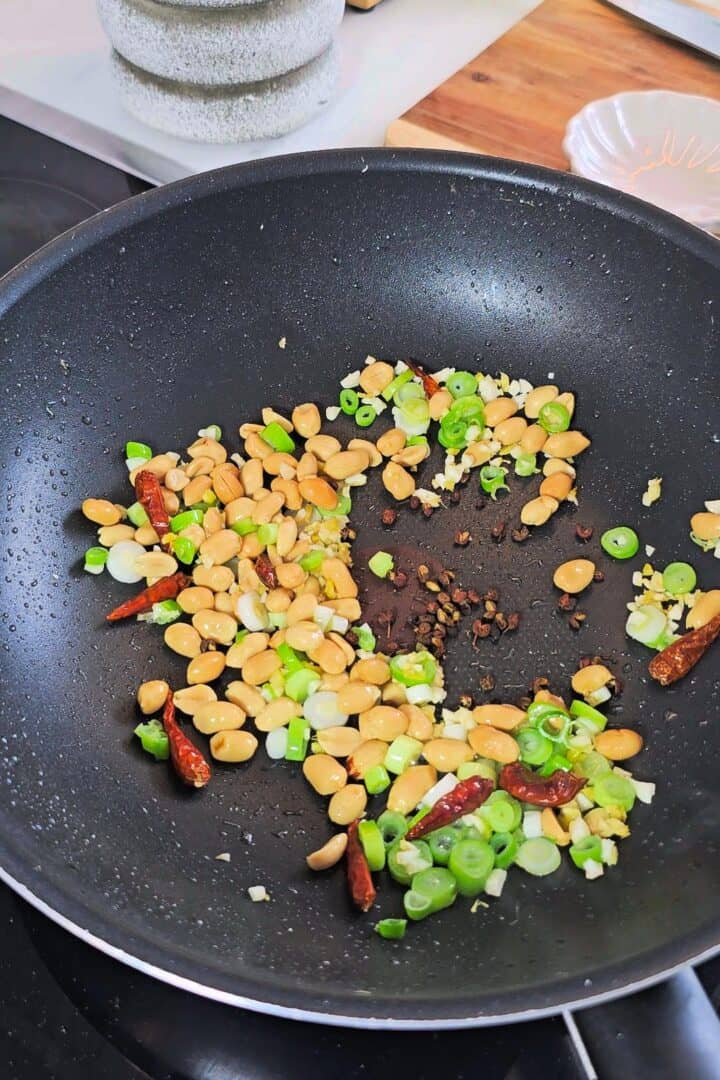Aromatics, dried chilies and roasted peanuts in a black wok.