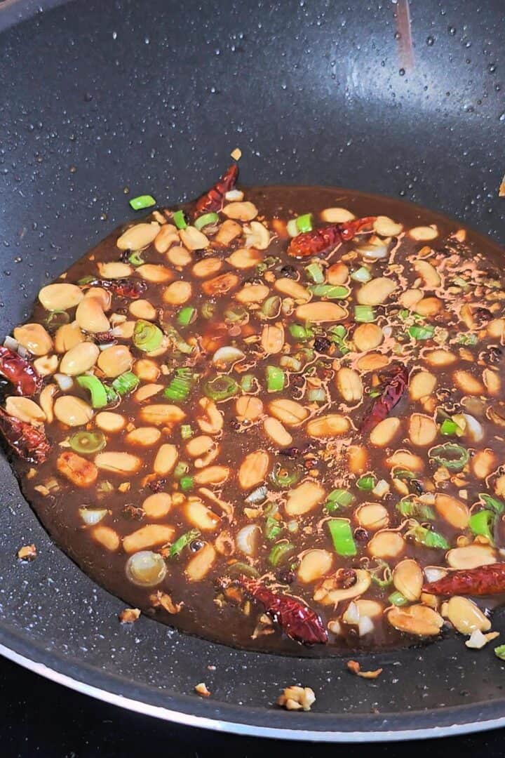 Kung sauce with peanuts, scallions and dried chilies in a black wok.