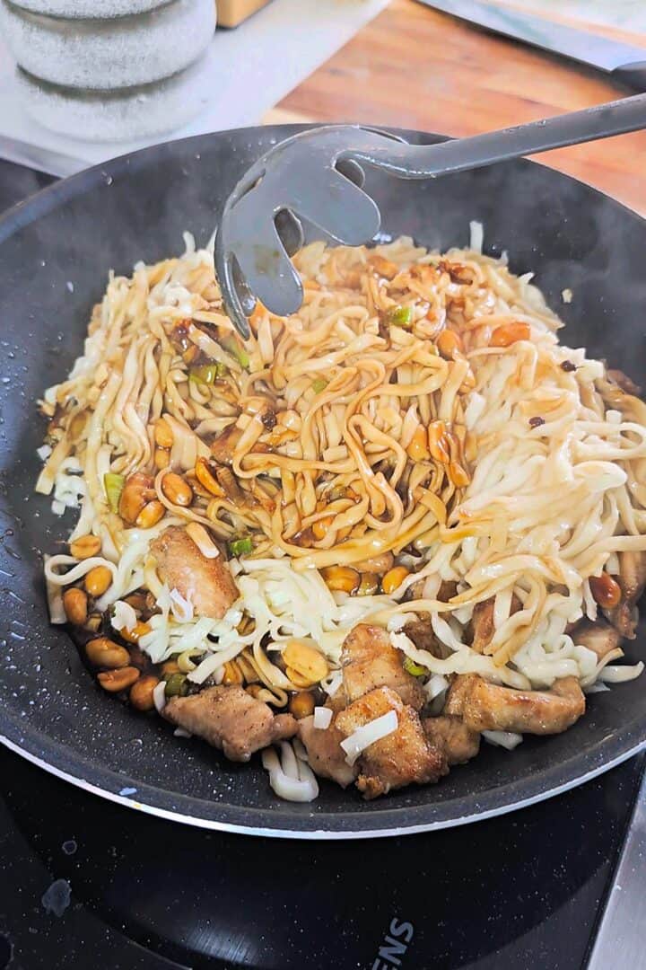 Noodles, chicken and peanuts in a wok.