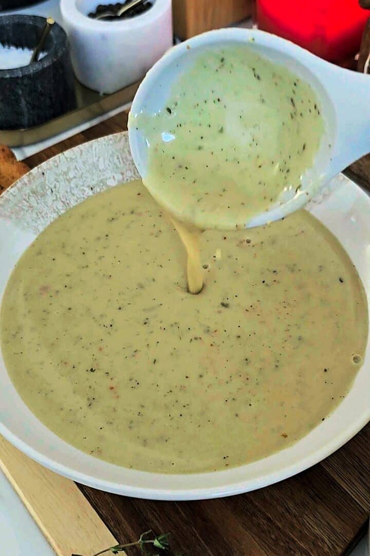 Ladle pouring the finished garlic soup into a bowl.