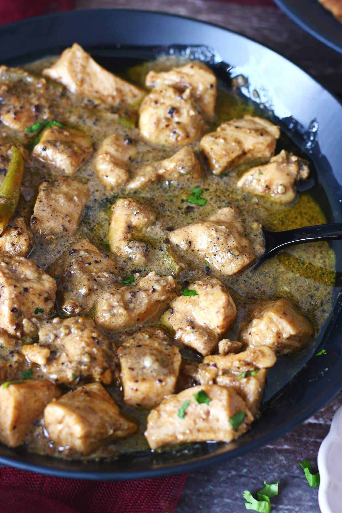 Close-up of chicken kali mirch in a creamy black pepper sauce garnished with cilantro.