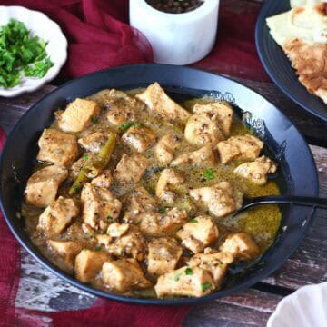Chicken Kali Mirch served in a black bowl with a side of roti, fresh cilantro, and a marble black pepper grinder in the background.
