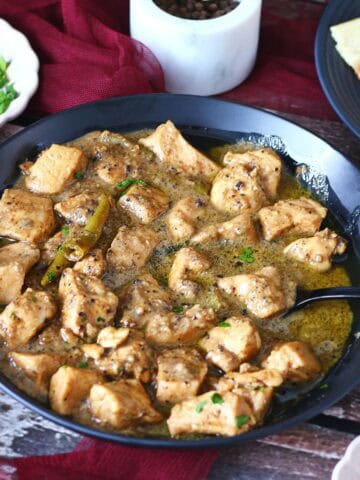 Chicken Kali Mirch served in a black bowl with a side of roti, fresh cilantro, and a marble black pepper grinder in the background.