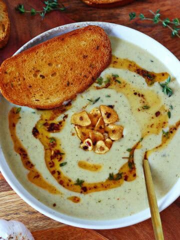 Creamy roasted garlic soup with garlic chips and chili oil on top.