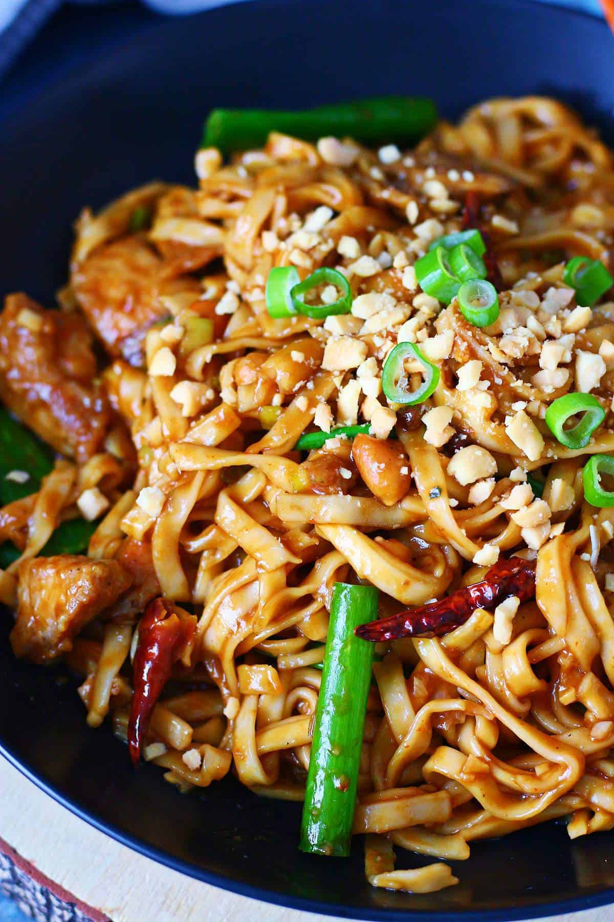 Close-up of Kung Pao chicken noodles with scallion greens and chopped peanuts garnish.