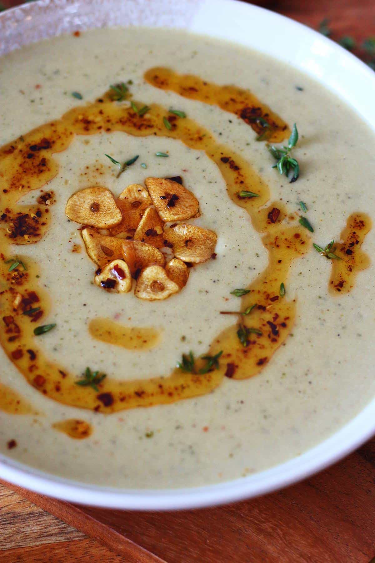 Close-up of roasted garlic soup showing garlic chips, chili oil, and thyme.