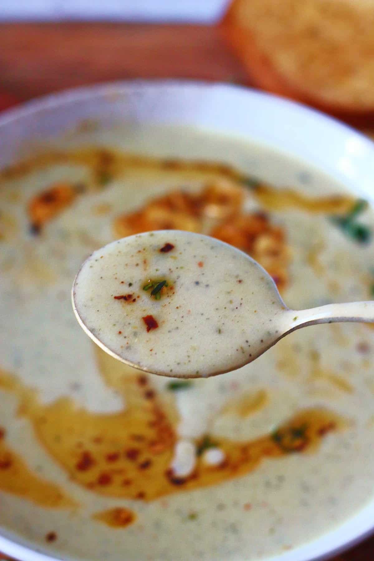 A spoonful of roasted garlic soup held above the bowl.