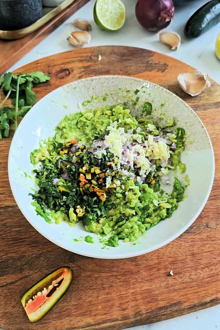 Bowl of mashed avocado mixed with red onion, jalapeรฑo, cilantro, garlic and lime for homemade guacamole.