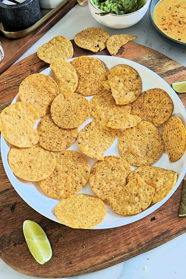 Round tortilla chips arranged in a single layer on a white baking dish.