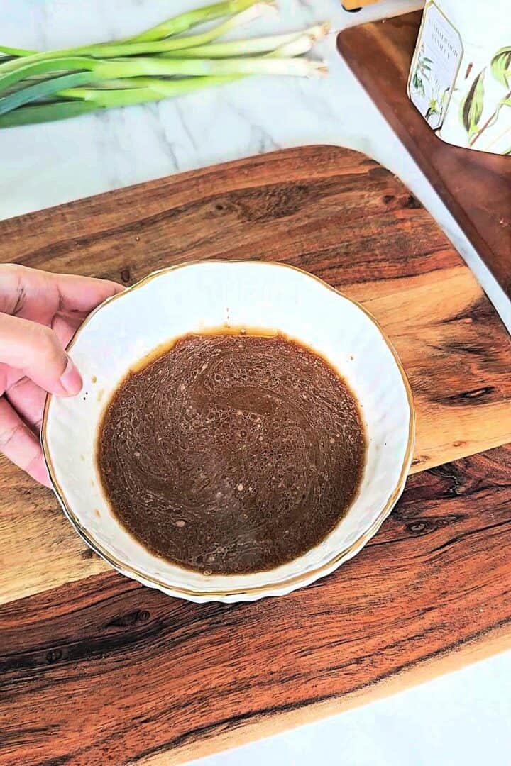 Bowl of prepared Chinese garlic sauce mixture being held over a wooden board.