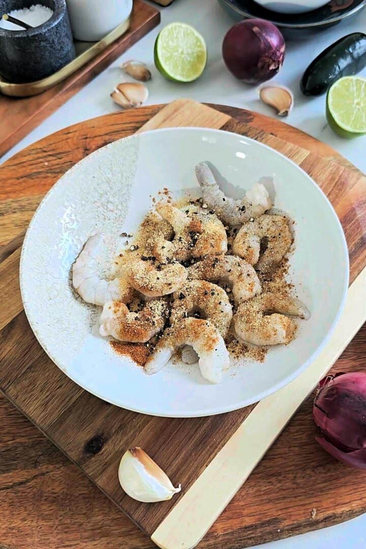 Raw shrimp in a bowl seasoned with garlic powder, smoked paprika, cayenne, black pepper and salt.