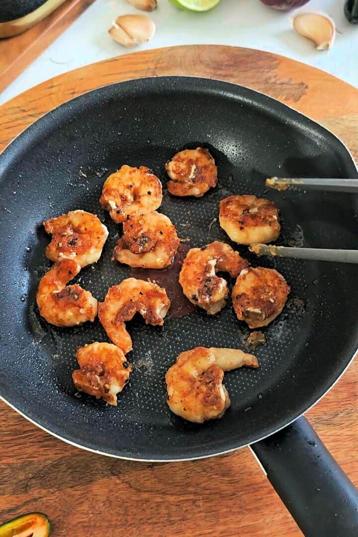 Seasoned shrimp being pan-fried in a skillet until golden and crispy.