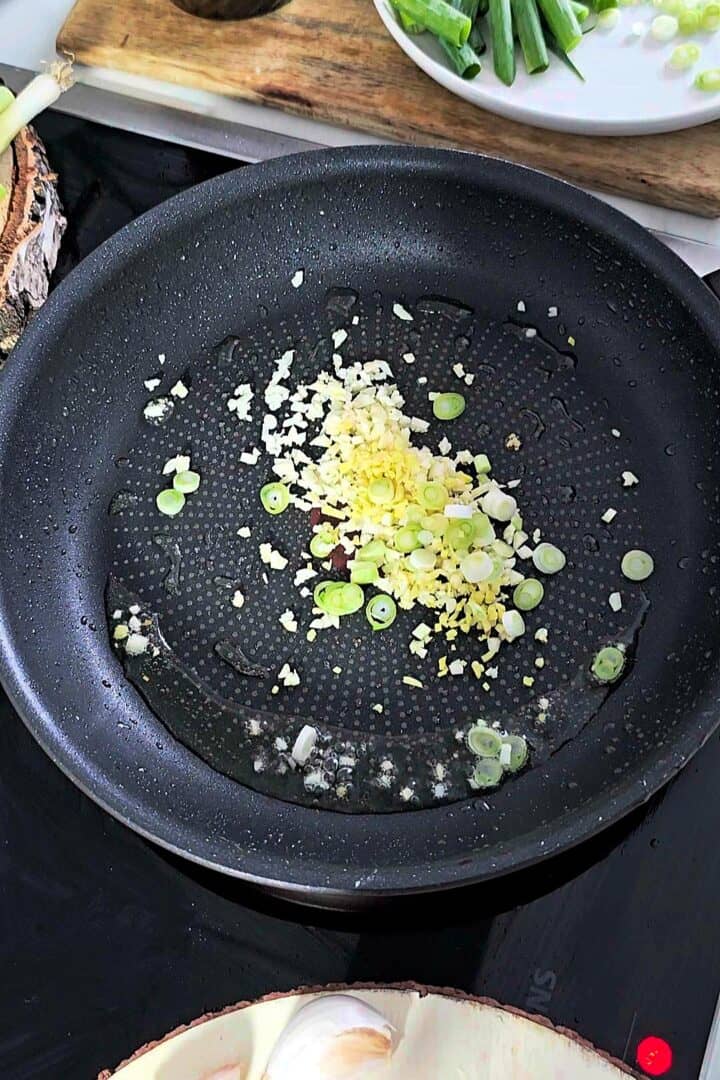 Minced garlic, ginger, and sliced scallions sautรฉing in a hot pan.