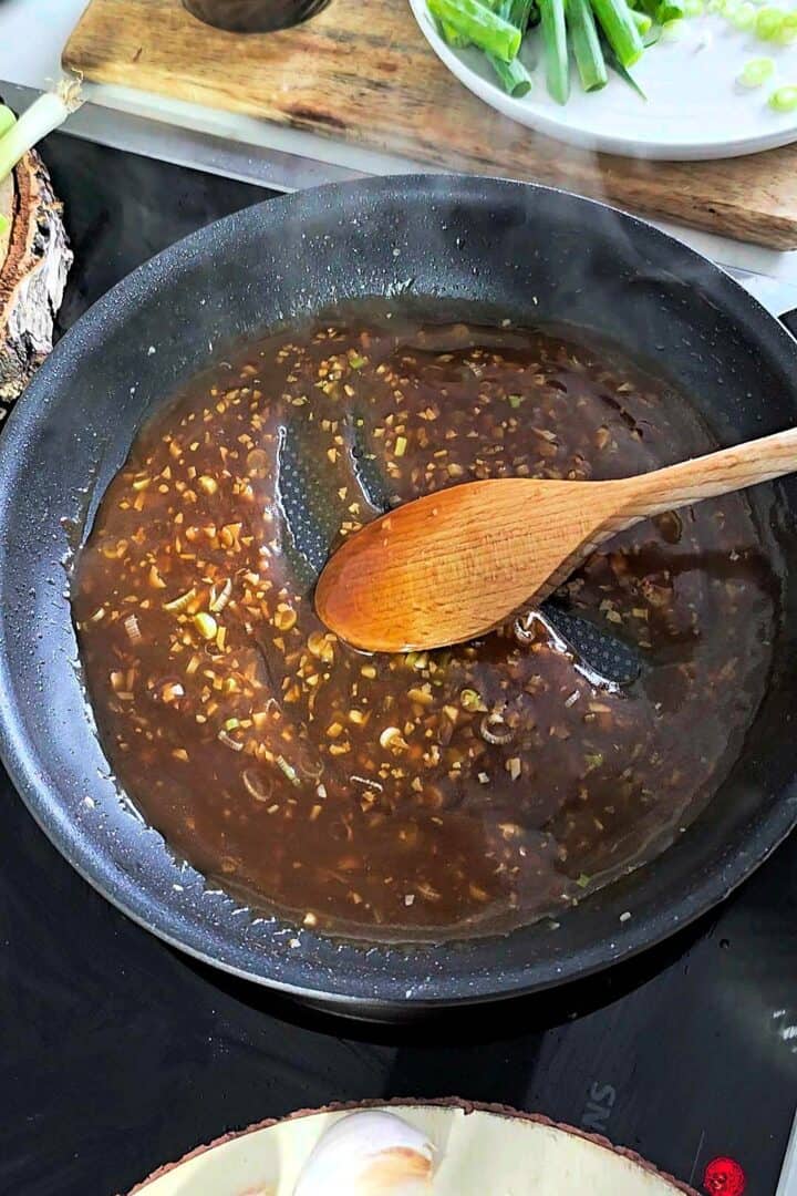 Garlic sauce simmering in a pan with a wooden spoon stirring it.
