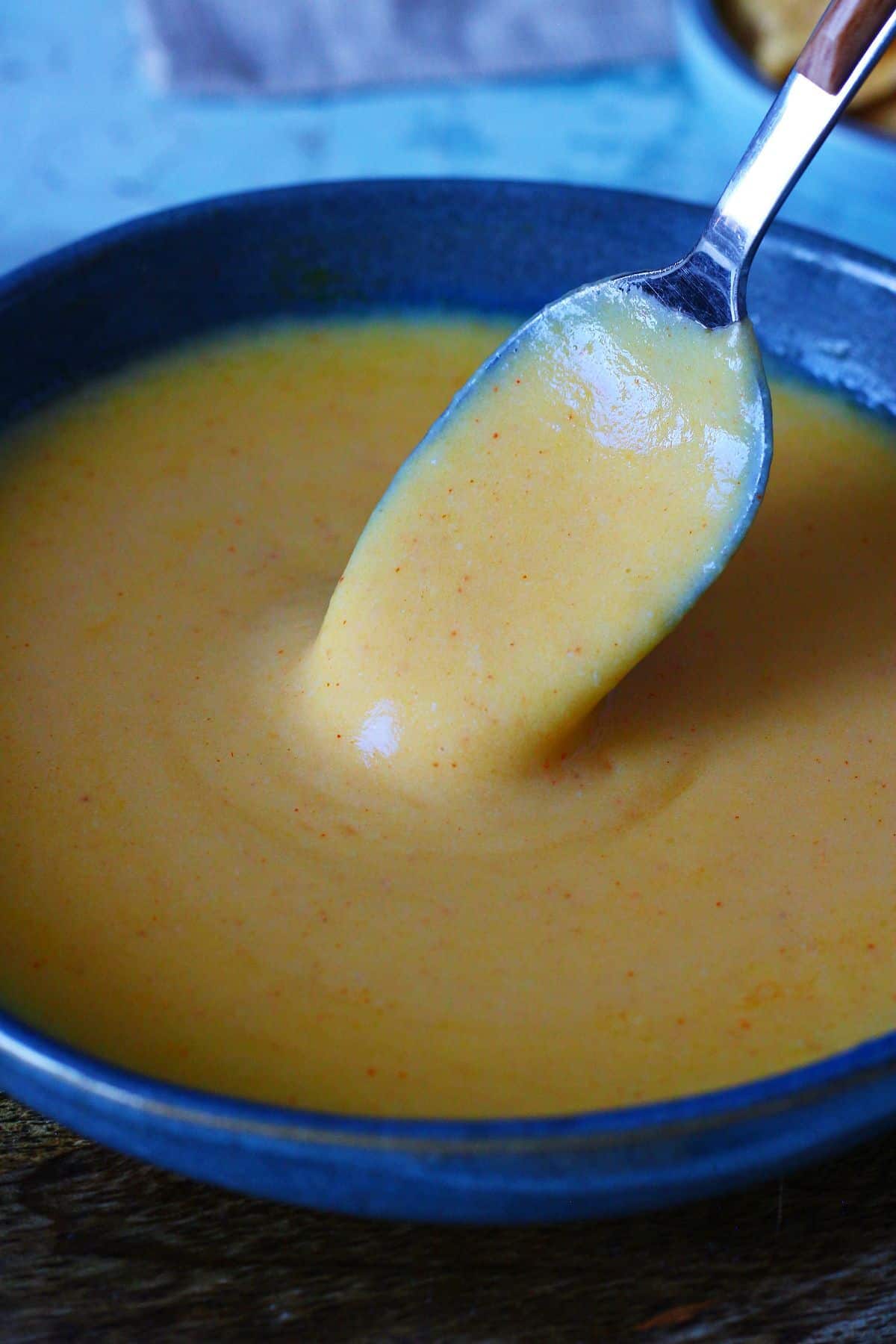 Smooth microwave cheese sauce with a spoon lifting the creamy sauce.