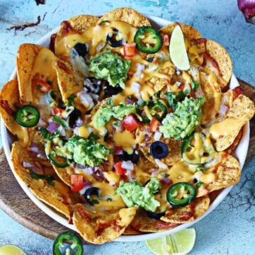 Oven-baked veggie nachos with melted cheese, fresh toppings, and guacamole served in a white dish.