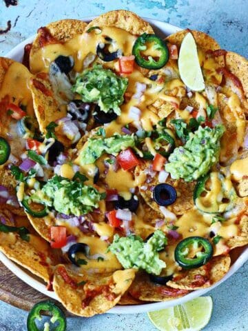 Oven-baked veggie nachos with melted cheese, fresh toppings, and guacamole served in a white dish.