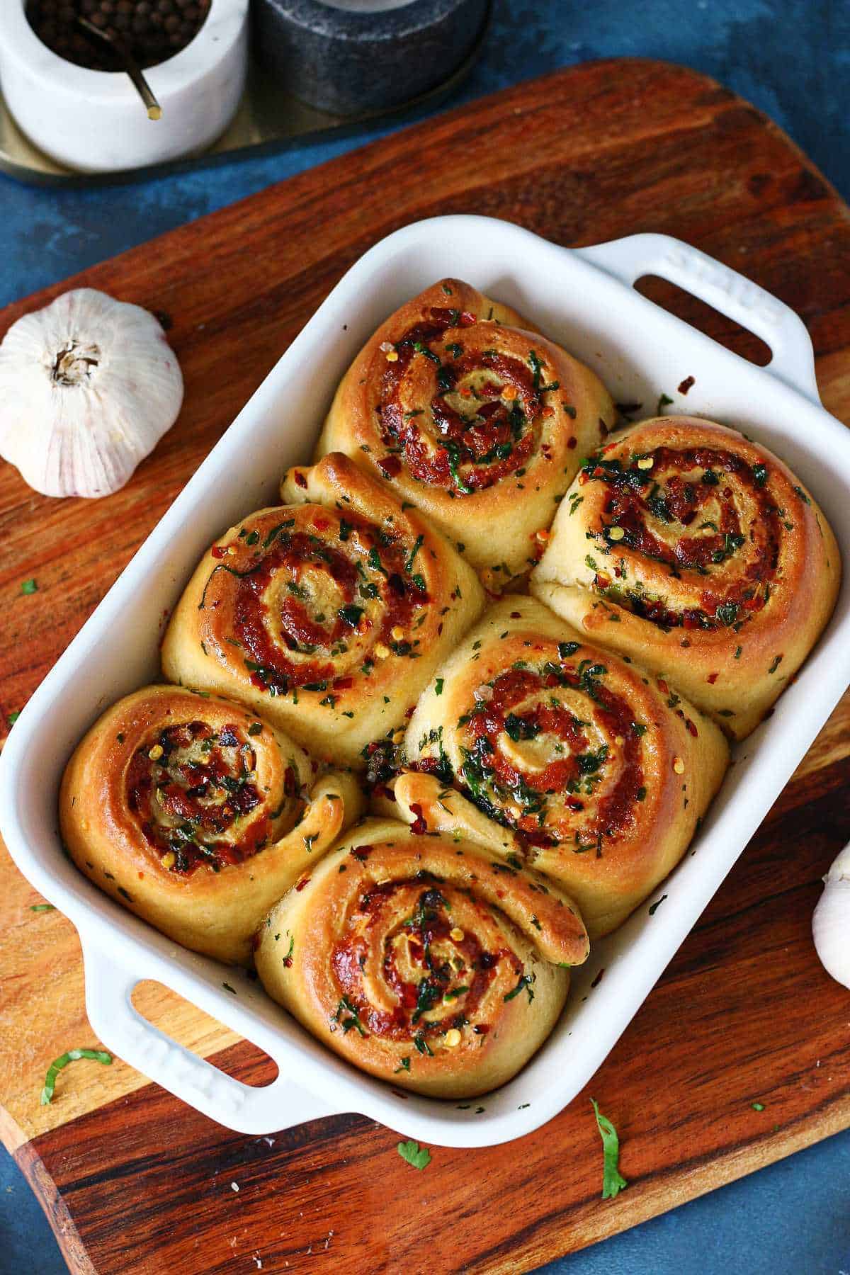 Baked garlic rolls arranged in a white ceramic dish on a wooden board.
