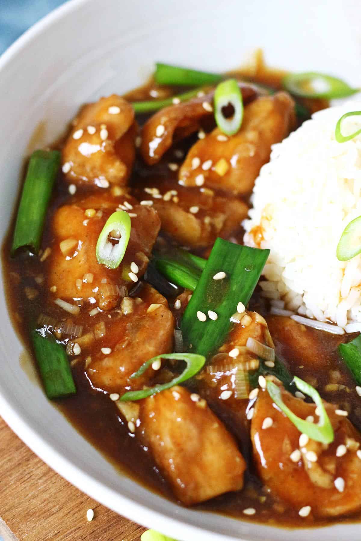 Close-up of Chinese chicken with garlic sauce, topped with scallions and sesame seeds.