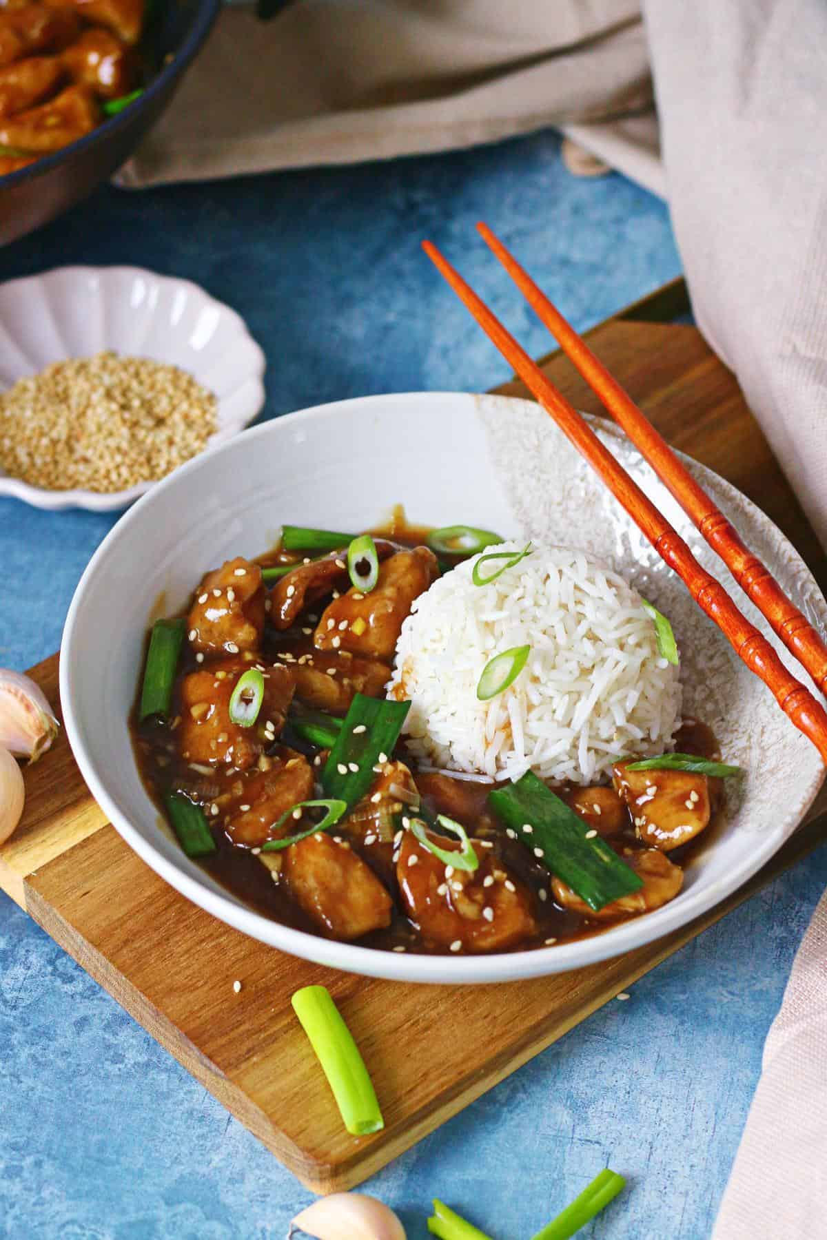 Bowl of Chinese chicken with garlic sauce served with rice, scallions, and sesame seeds.