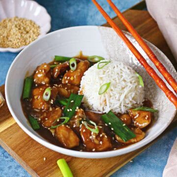Chinese chicken with garlic sauce in a bowl with rice, chopsticks, and sesame seeds.