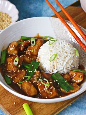 Chinese chicken with garlic sauce in a bowl with rice, chopsticks, and sesame seeds.