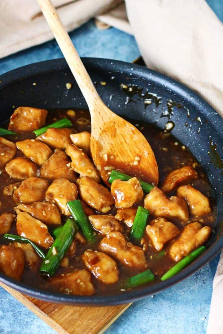 Chinese chicken with garlic sauce cooking in a pan with scallions and a wooden spoon.