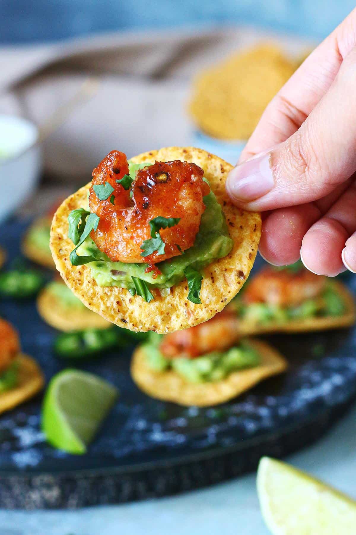 Hand holding a mini shrimp tostada topped with guacamole and cilantro.