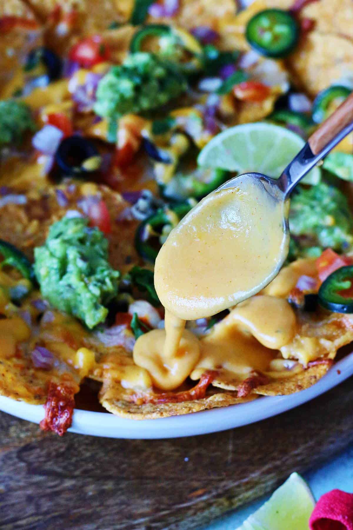 Cheese sauce being drizzled over loaded veggie nachos with guacamole and fresh toppings.