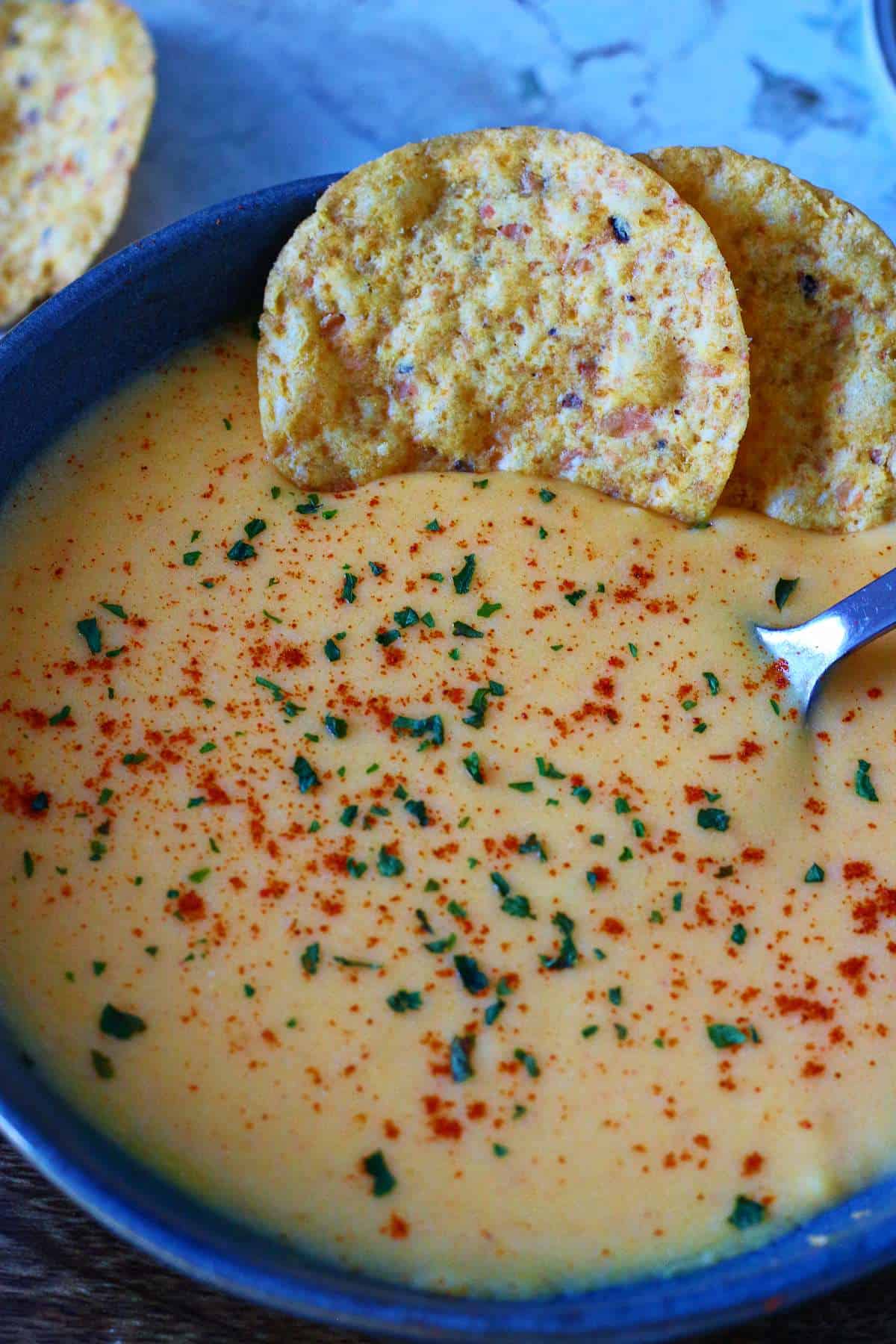 Close-up of creamy microwave cheese sauce with smoked paprika and dried parsley showing smooth texture.