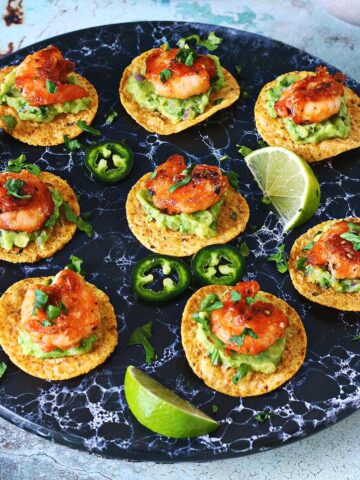 Mini shrimp tostadas on a black serving plate topped with guacamole, shrimp and cilantro.