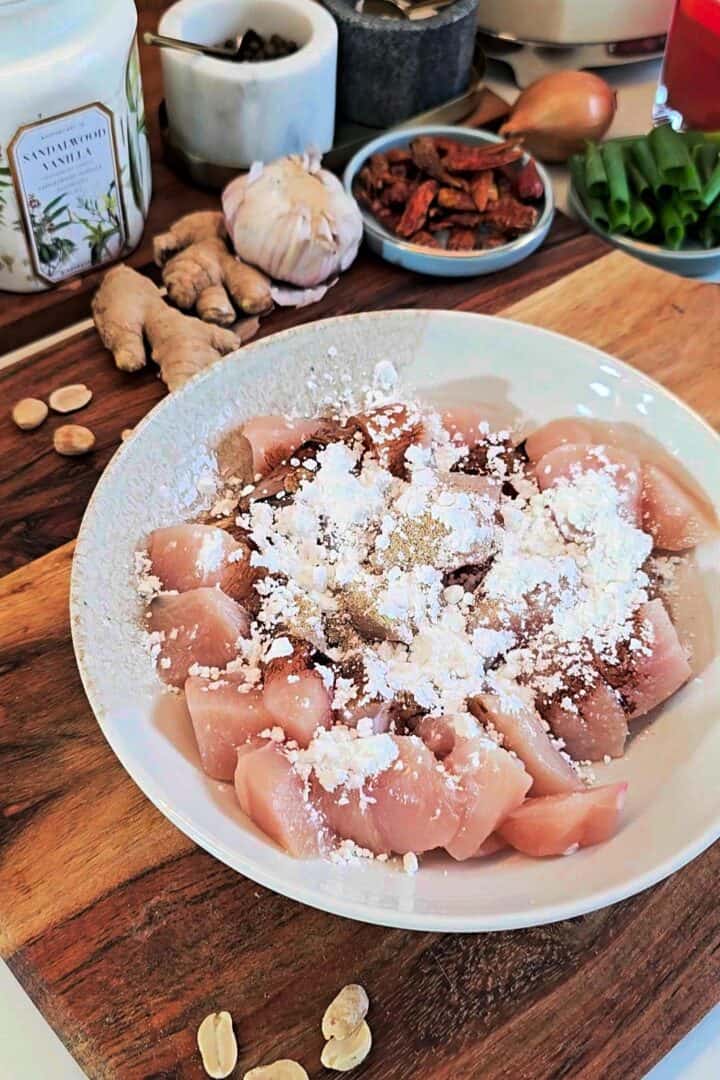 Raw chicken pieces coated with cornstarch and seasonings in a bowl.