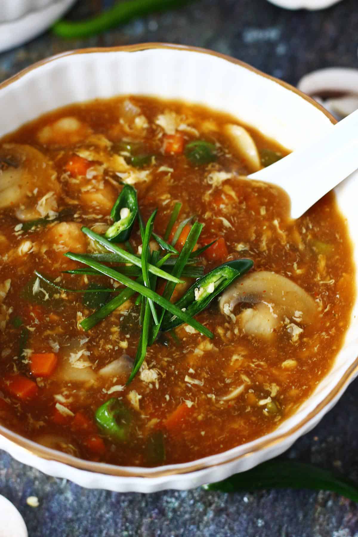 Close-up of 19b soup with vegetables, egg strands, and green chili slices in a white bowl.