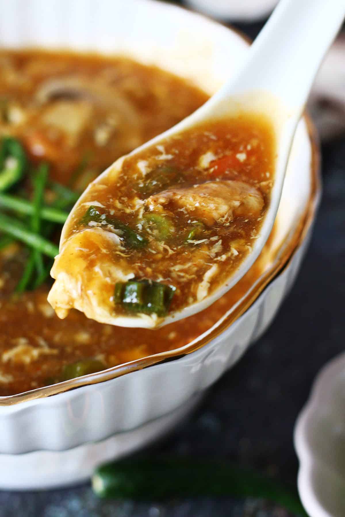 White spoon holding 19b soup with visible vegetables and egg strands.