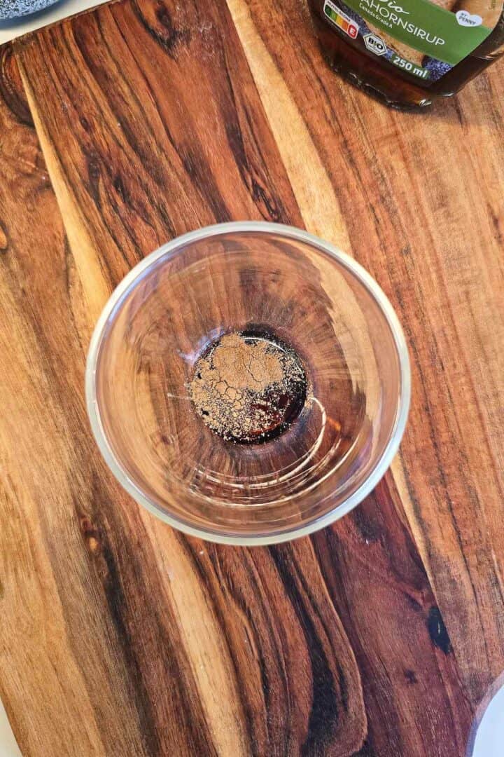 Ground cinnamon sprinkled over maple syrup inside a clear glass.