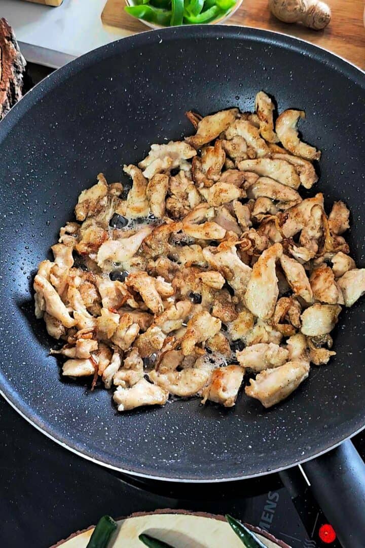 Thinly sliced chicken stir-frying in a wok until lightly browned.