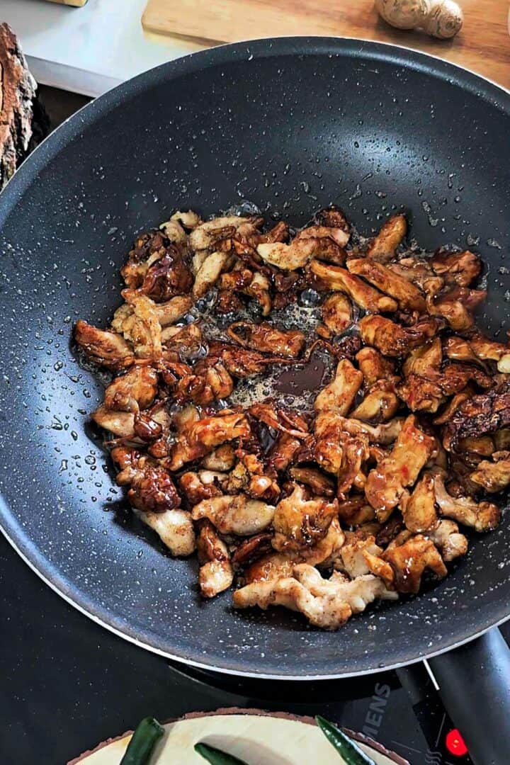 Chicken tossed with soy sauce, oyster sauce, chili garlic ketchup, and sugar in the wok.