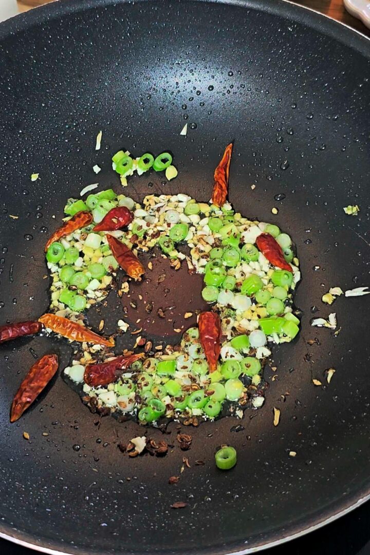 Chopped scallions, dried red chilies, garlic, and spices sautéing in oil.