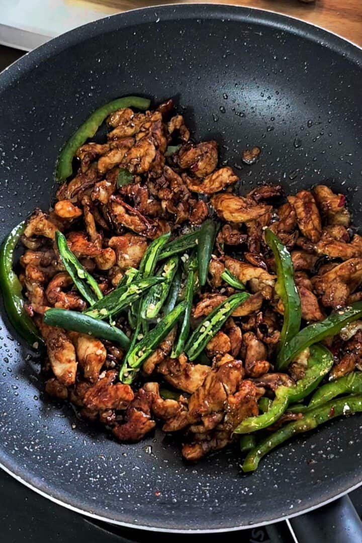 Green chilies and bell pepper added to the sauced chicken in the wok.