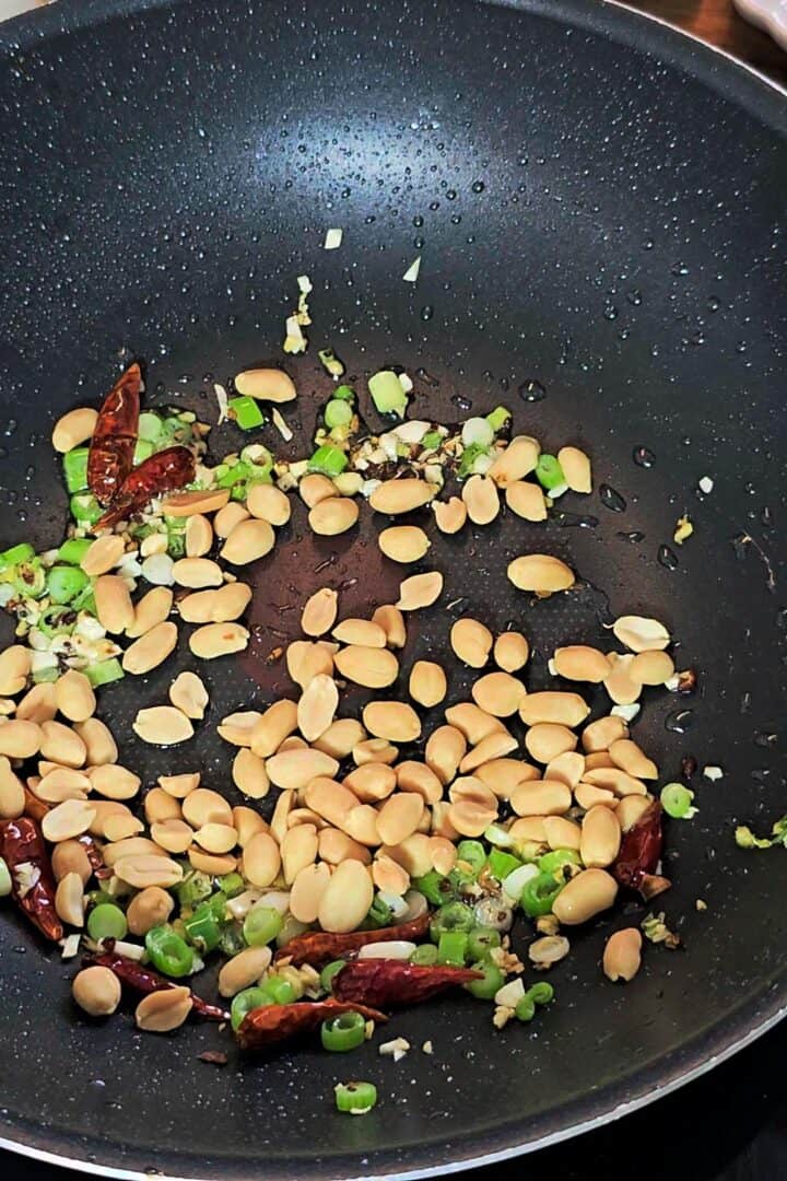 Peanuts toasting in a pan with aromatics and dried chilies.