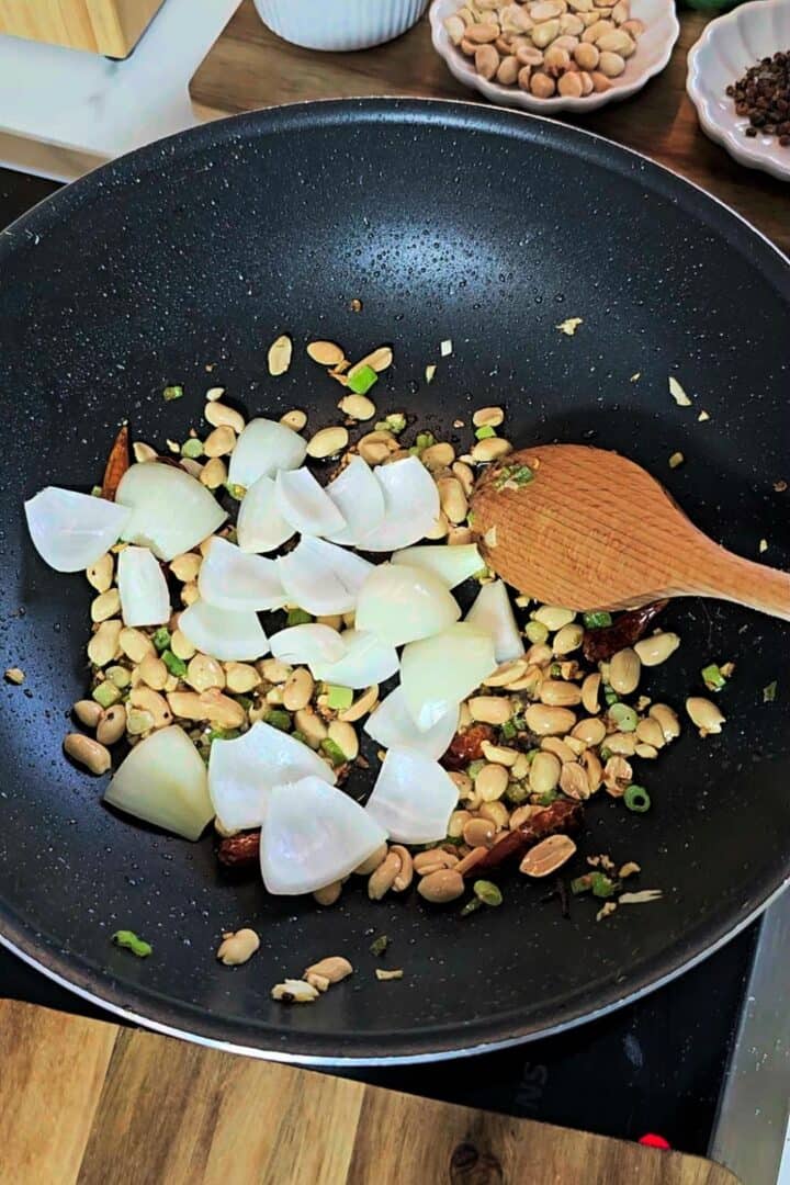 Onion chunks added to peanuts and aromatics in a pan.
