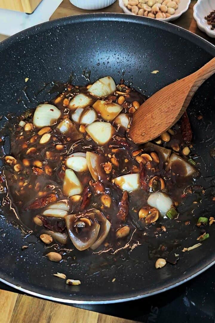 Dark sauce simmering in a pan with peanuts and onion.