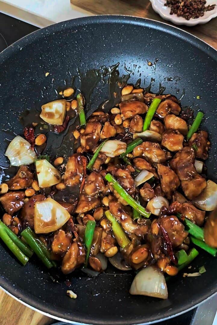 Cooked chicken combined with sauce, peanuts, and scallions in a pan.