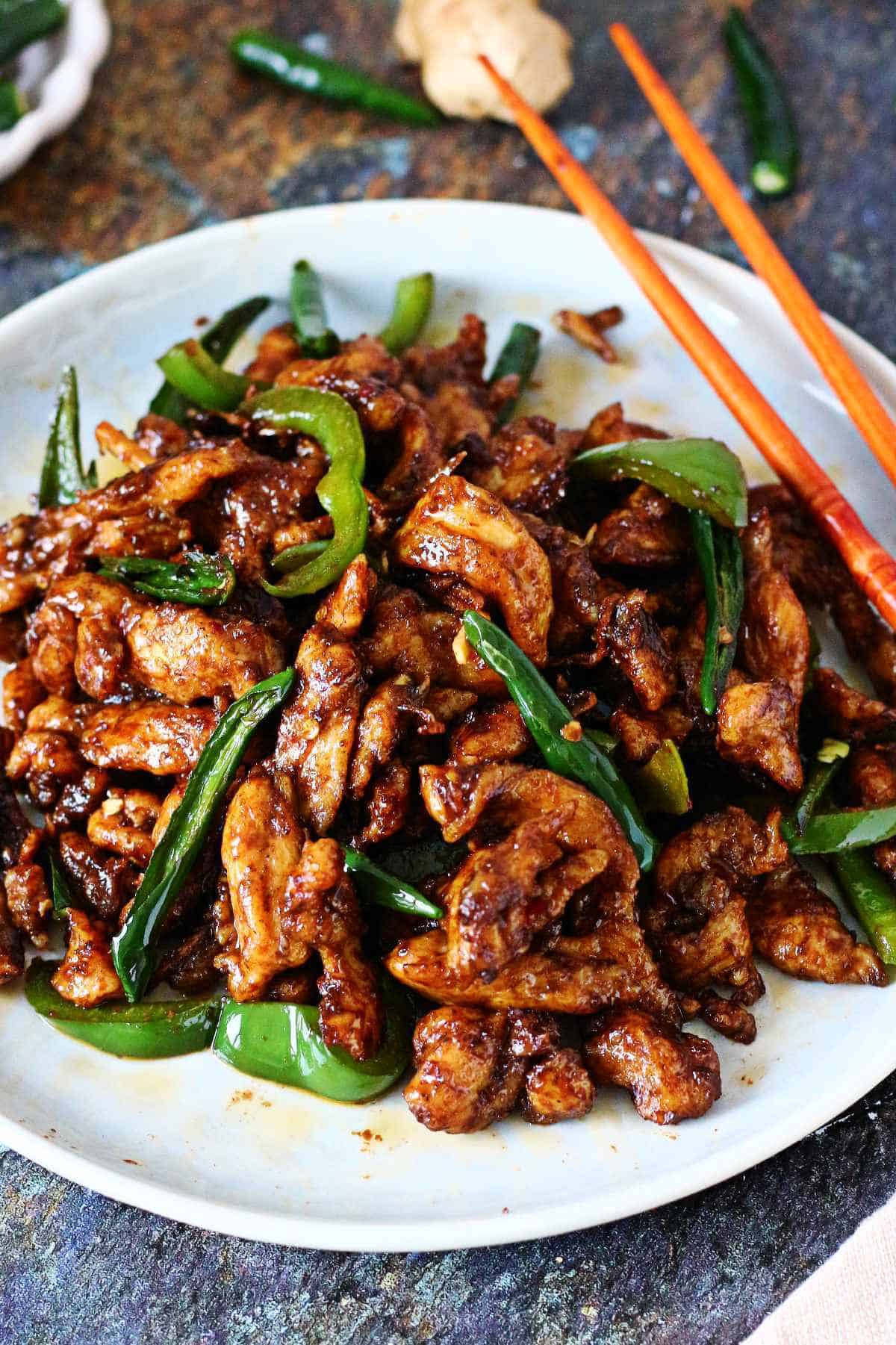 Styled plate of Chinese Chicken Chili Dry with chopsticks, green chilies, and ginger in the background.