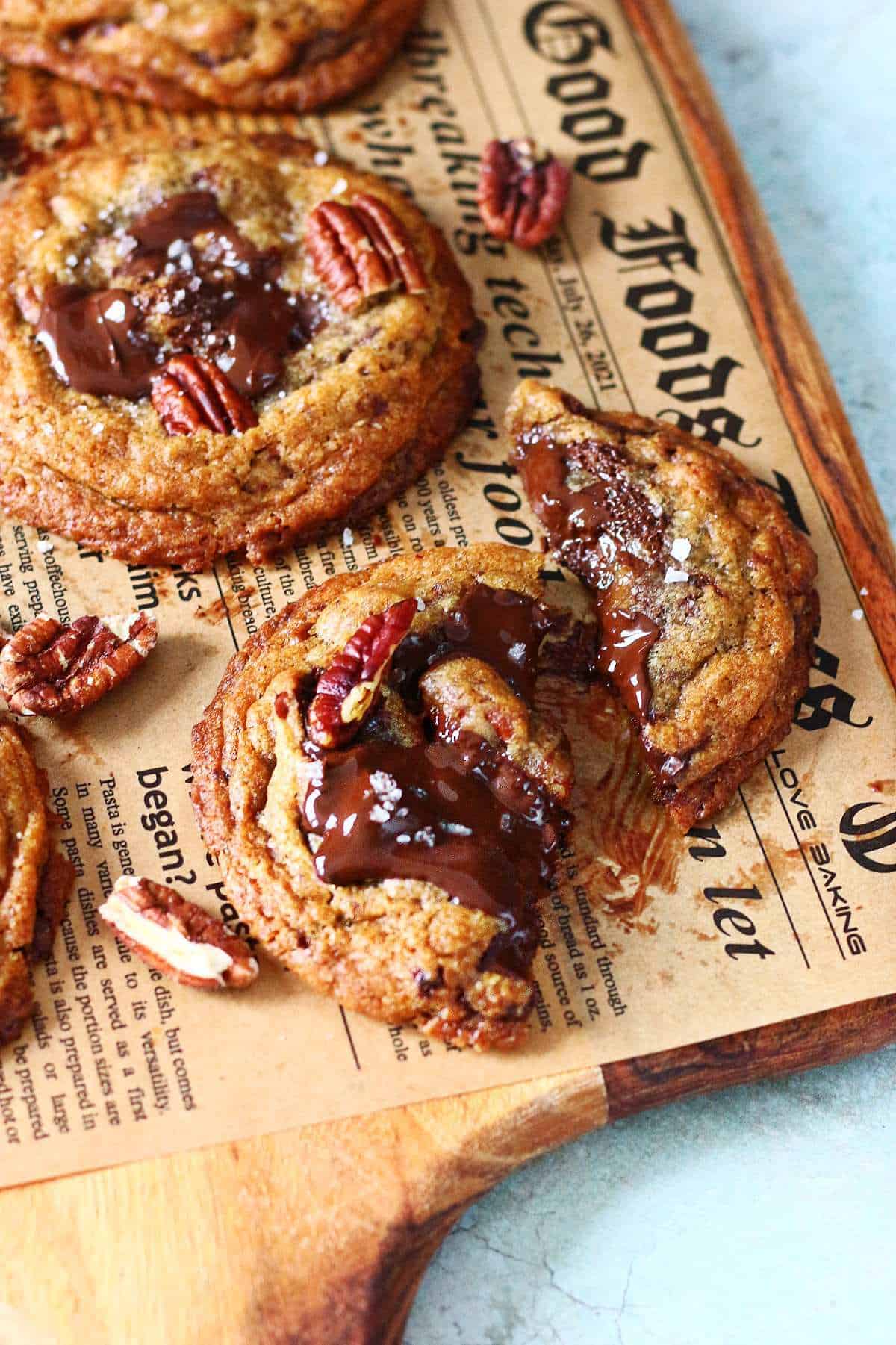 Chocolate chip pecan cookie broken in half, showing a gooey dark chocolate center with toasted pecans and crisp edges.