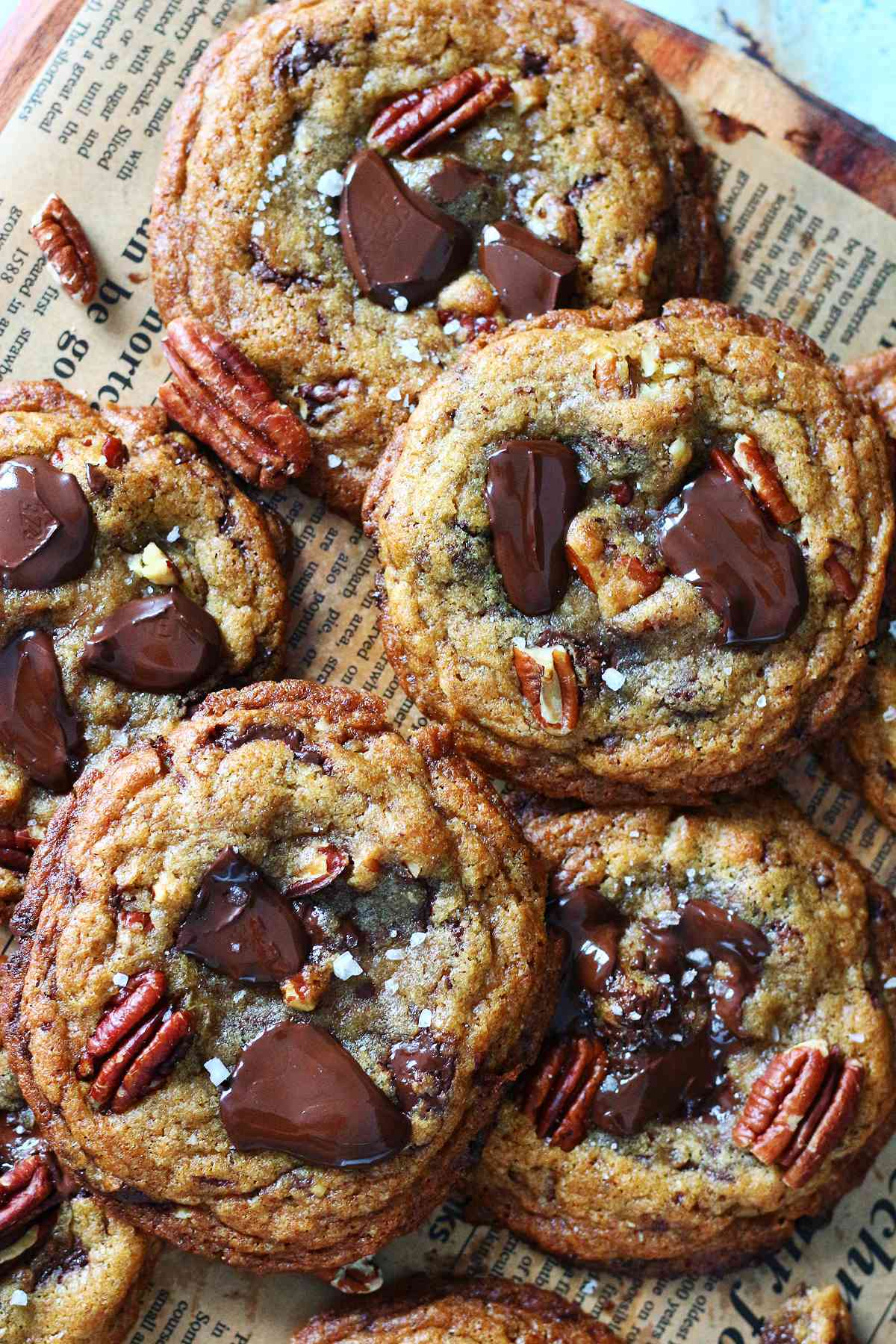 Overlapping chocolate chip pecan cookies with melted dark chocolate chunks, toasted pecans, and a sprinkle of flaky sea salt on parchment paper.