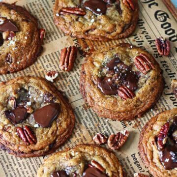 Overhead view of chocolate chip pecan cookies with melted dark chocolate, pecan halves, and flaky sea salt on parchment paper.