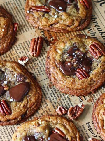 Overhead view of chocolate chip pecan cookies with melted dark chocolate, pecan halves, and flaky sea salt on parchment paper.