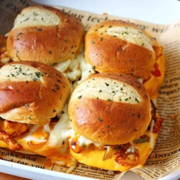 Chicken fajita sliders arranged in a baking dish with melted cheese, garlic butter-brushed brioche buns, and visible bell peppers.